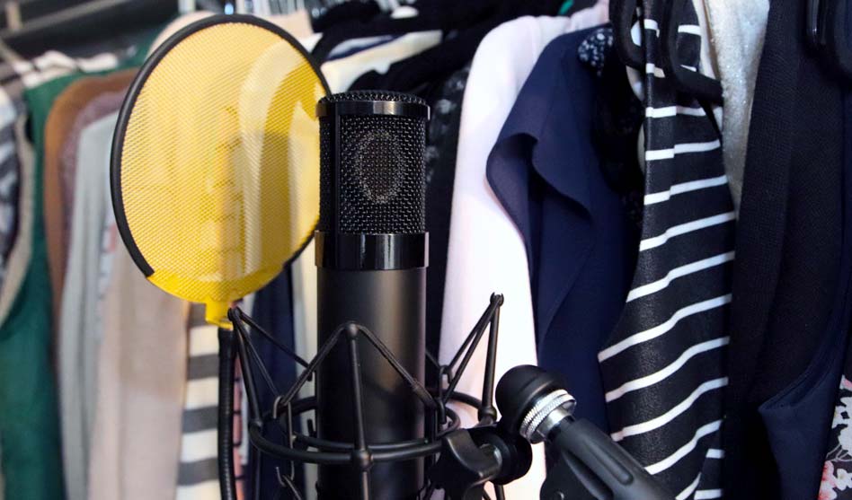 Microphone with yellow pop filter in closet with hanging cloths